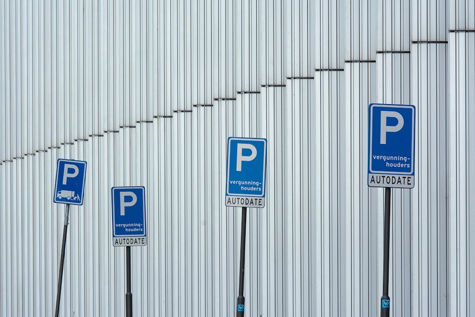 Four blue parking permits with white lettering are mounted on black metal poles against a silver corrugated metal wall. Each permit displays a large 'P' symbol, with smaller text reading 'vergunning-houders' and 'AUTODATE' beneath. The permits are arranged in a descending order from right to left, with the tallest permit positioned on the far right and the shortest on the far left. The permits are part of a parking management system, likely related to house removals or moving logistics, as suggested by the context of [COMPANY_NAME]'s services. The image showcases designated parking permit areas for loading and unloading activities, which are essential for the efficient and legal execution of home relocation projects, particularly in urban settings such as Tower Hamlets. The overall scene emphasizes compliance with parking permits and local regulations during furniture transport or moving processes, with natural lighting highlighting the details of the permits and wall surfaces.